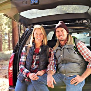 Couple Sitting on Car, Outdoors in Nature, Smiling, Wearing Vests and Hats