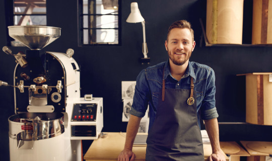Man Smiling, Coffee Shop, Machines in Background, Blue Wall