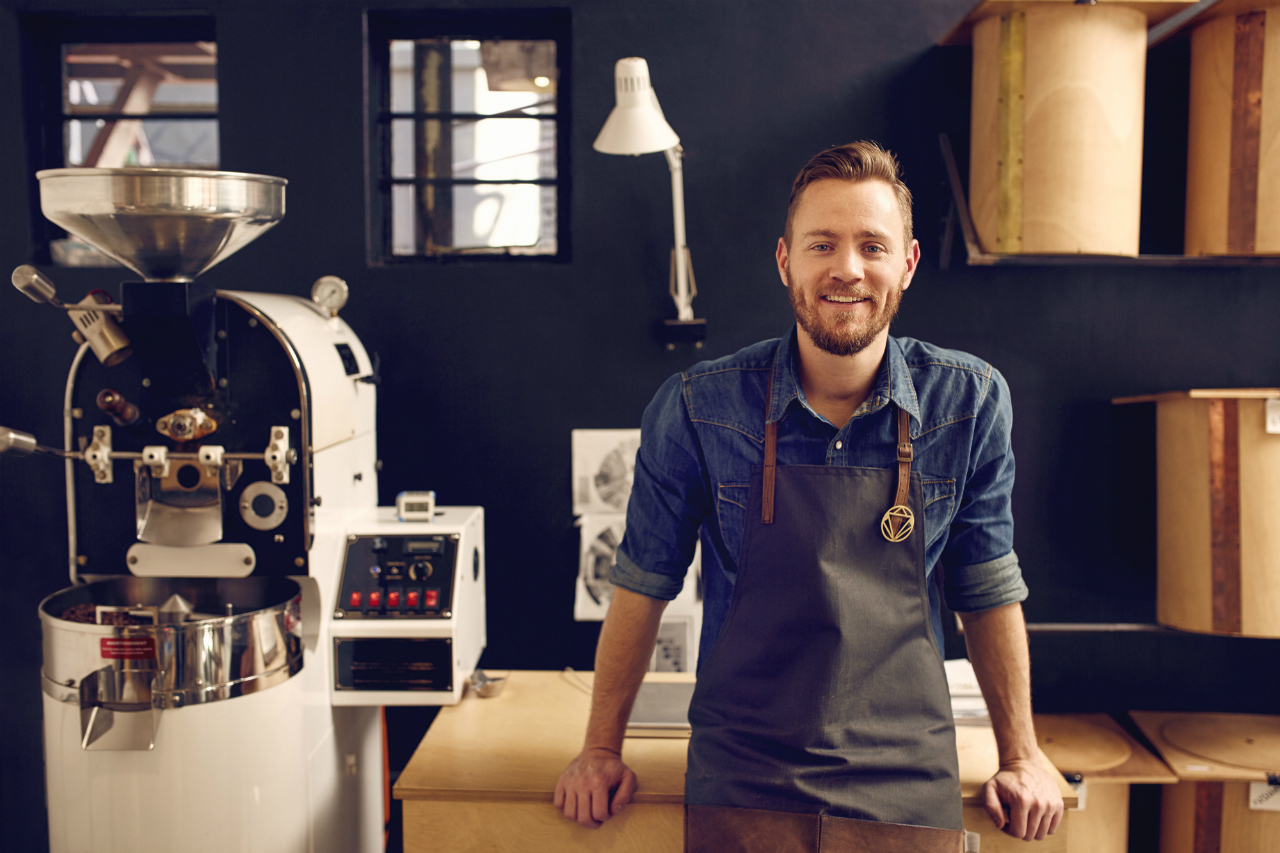 Man Smiling, Coffee Shop, Machines in Background, Blue Wall