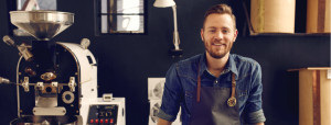Man Smiling, Coffee Shop, Machines in Background, Blue Wall
