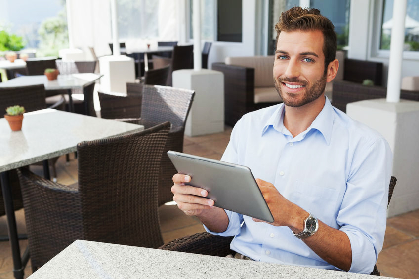 Man Smiling, Using a Tablet While at a Restaurant