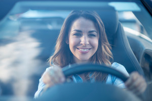 Woman Driving in Car, Smiling, Behind the Wheel, Blue Background