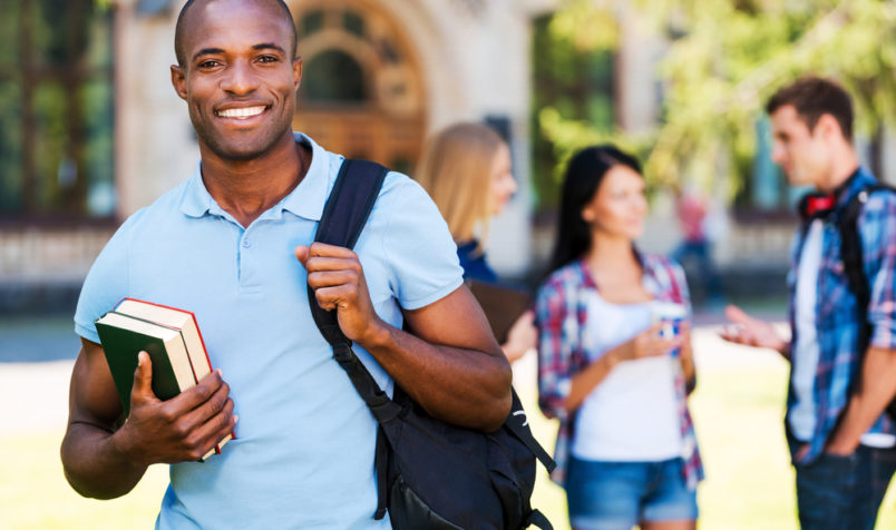 Student Smiling With Books, College Settings, Students in Background Conversing