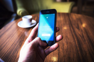 Man Holding Cellphone, Twitter, Cup of Coffee, Sitting at Table, Blurred Background