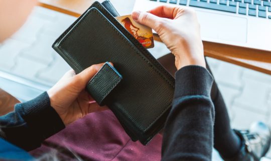 Woman sitting at a desk while pulling a credit card out of her black wallet