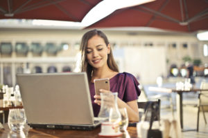 Woman at coffee shop with laptop, looking at cellphone