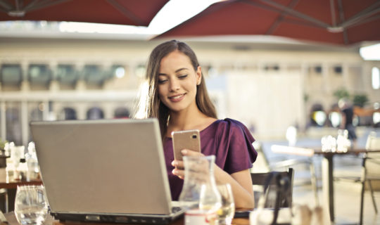 Woman at coffee shop with laptop, looking at cellphone