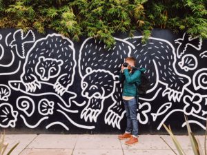 Young man holding a camera standing in front of a mural