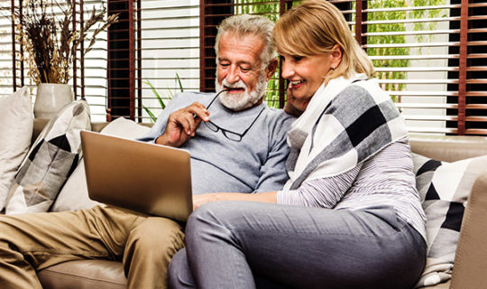 Two mature adults sitting on the sofa looking at their computer