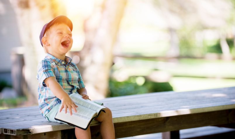 Laughing child sitting on a bench with a book