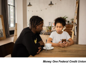 Two people at table, kitchen, holding phone, parent and child, discussing