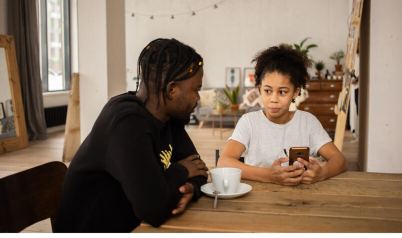 Two people at table, kitchen, holding phone, parent and child, discussing
